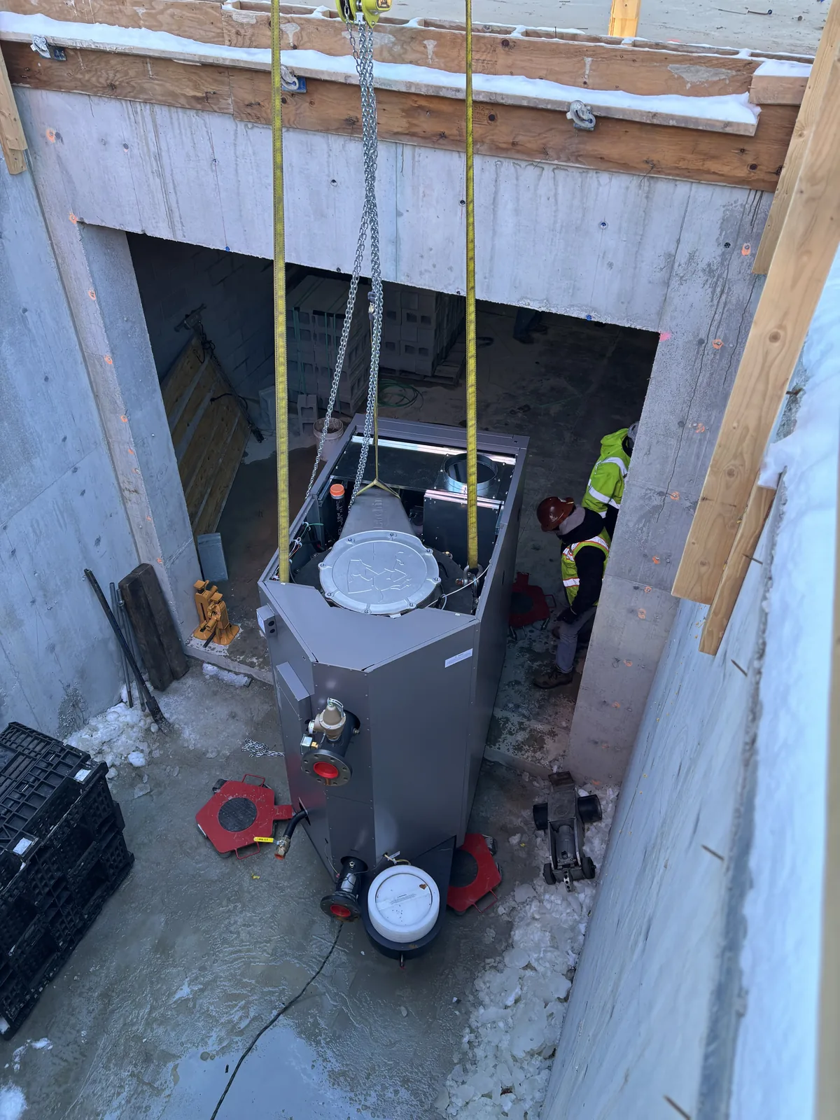 A large cylindrical mechanical vessel landed in a concrete shaft on lifting straps with workers alongside