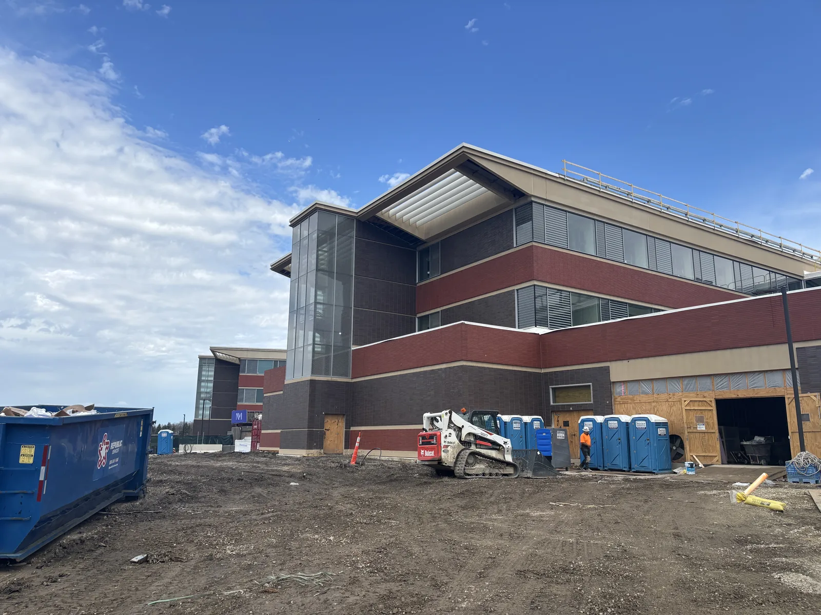 A new multi-storey healthcare building exterior on a clear day with construction dumpsters and site fencing in front