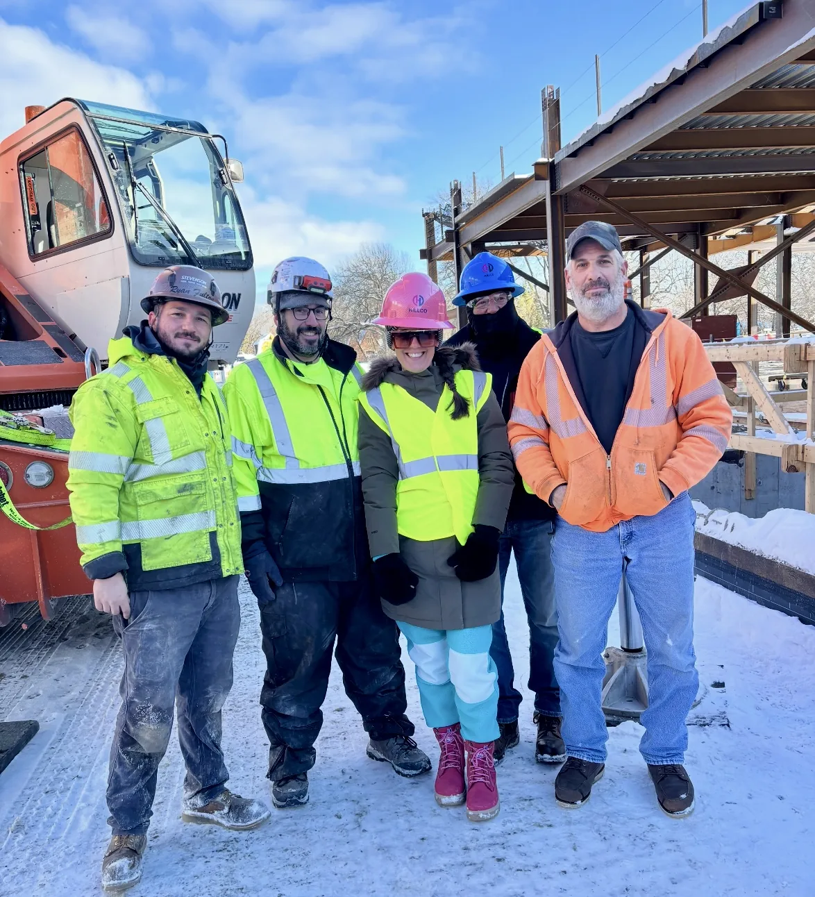 Nikki Liddy in a pink hard hat with four crew members in high-visibility jackets in front of a crane on a snowy jobsite