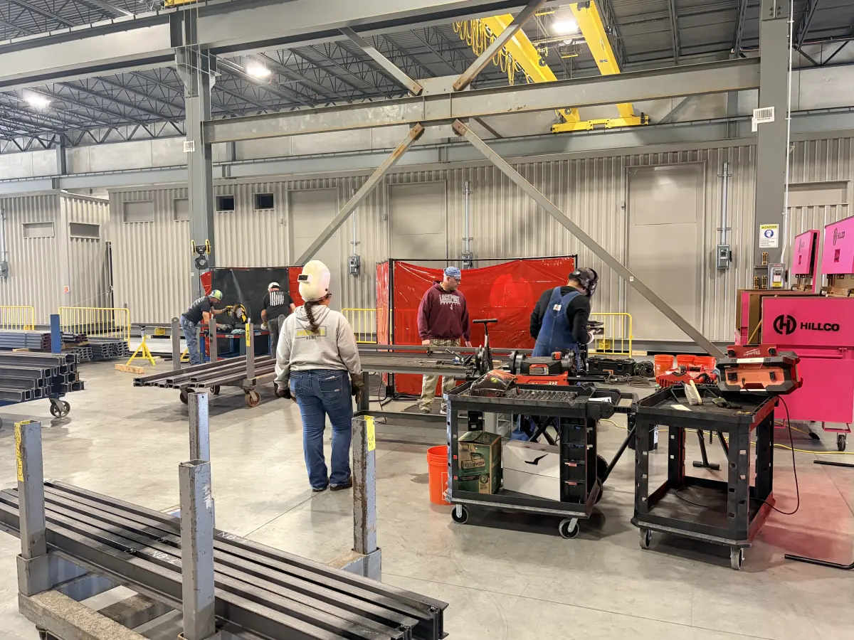 Hillco crew cutting and welding steel in a shop bay, with pink Hillco gang boxes on the right