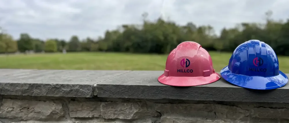 A pink and a blue Hillco hard hat side by side on a stone wall