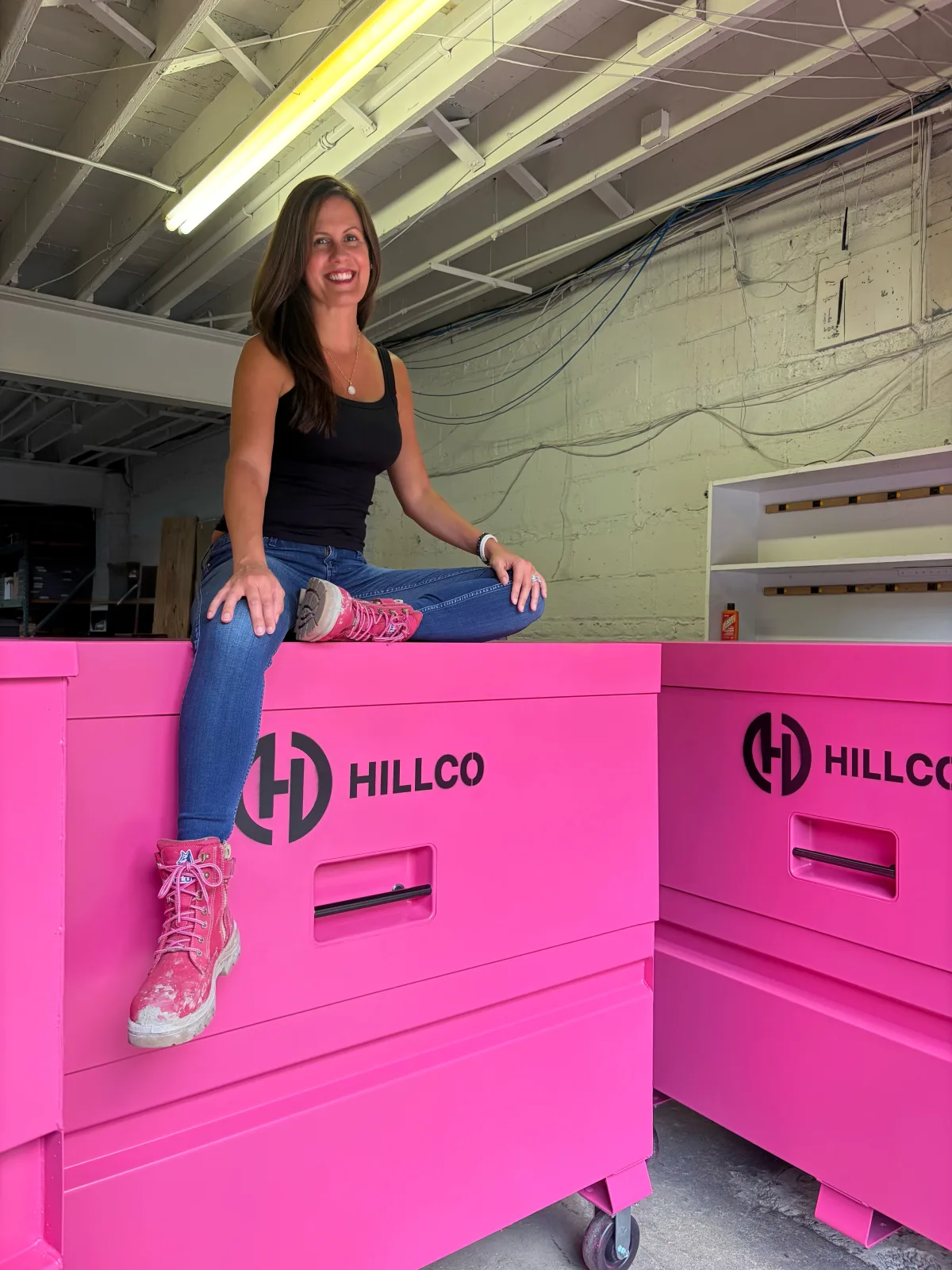 Nikki Liddy sitting on a pink Hillco gang box in the warehouse, pink work boots, smiling