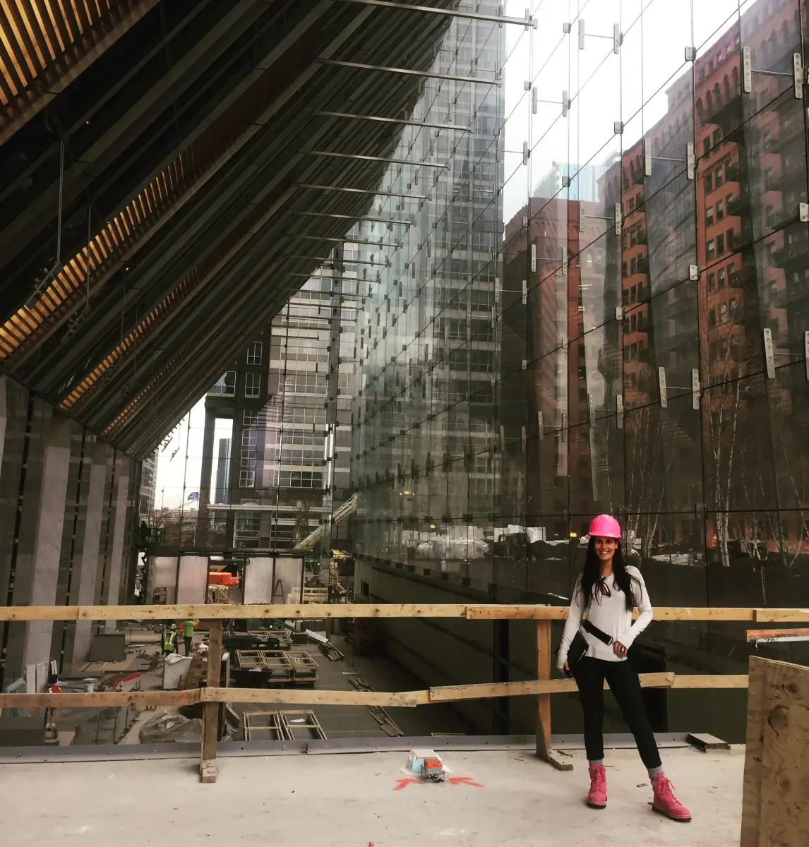 Nikki Liddy, owner of Hillco Distributing, in a pink hard hat and pink boots on the deck of a Chicago high-rise under construction, glass curtain wall behind her