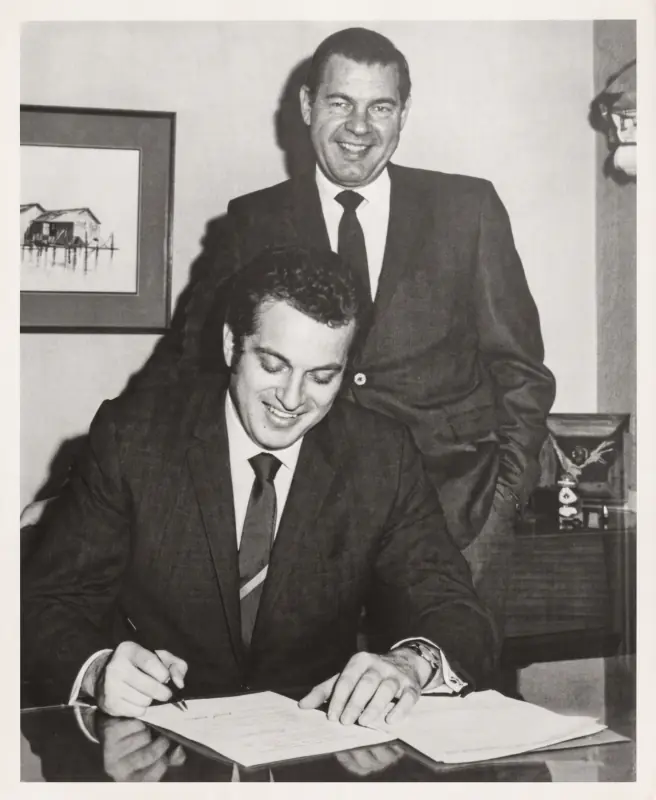Black and white photo from May 1970 of Ron Hillman, founder of Hillco Distributing, seated at a desk signing the Trane Wholesaler Program agreement